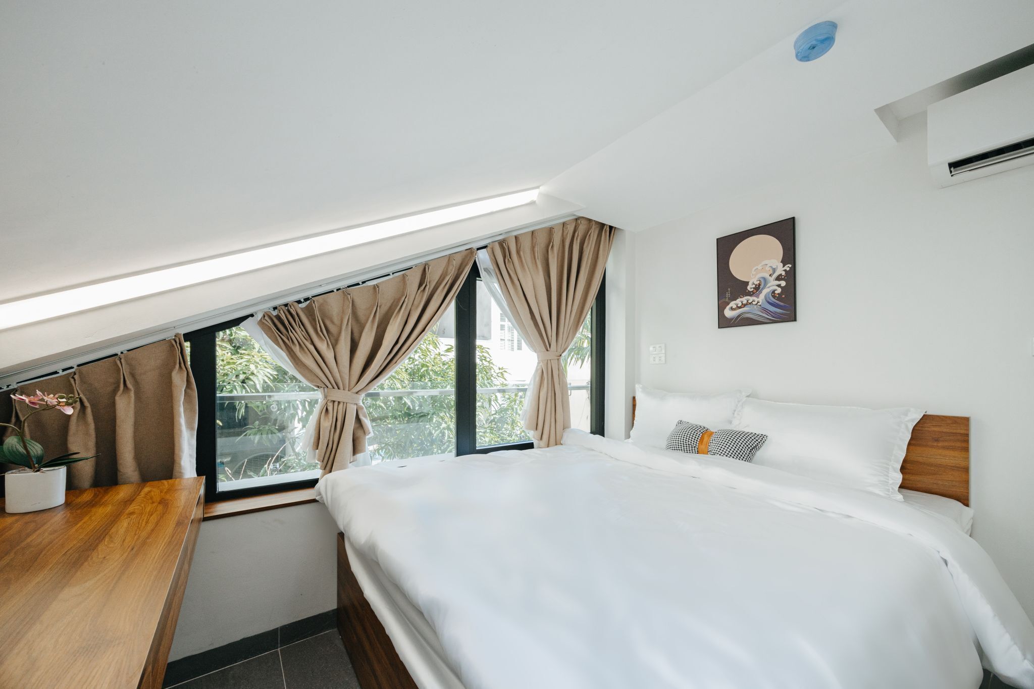 A modern bedroom with a large bed, a wooden desk, and a view of greenery through the window.
