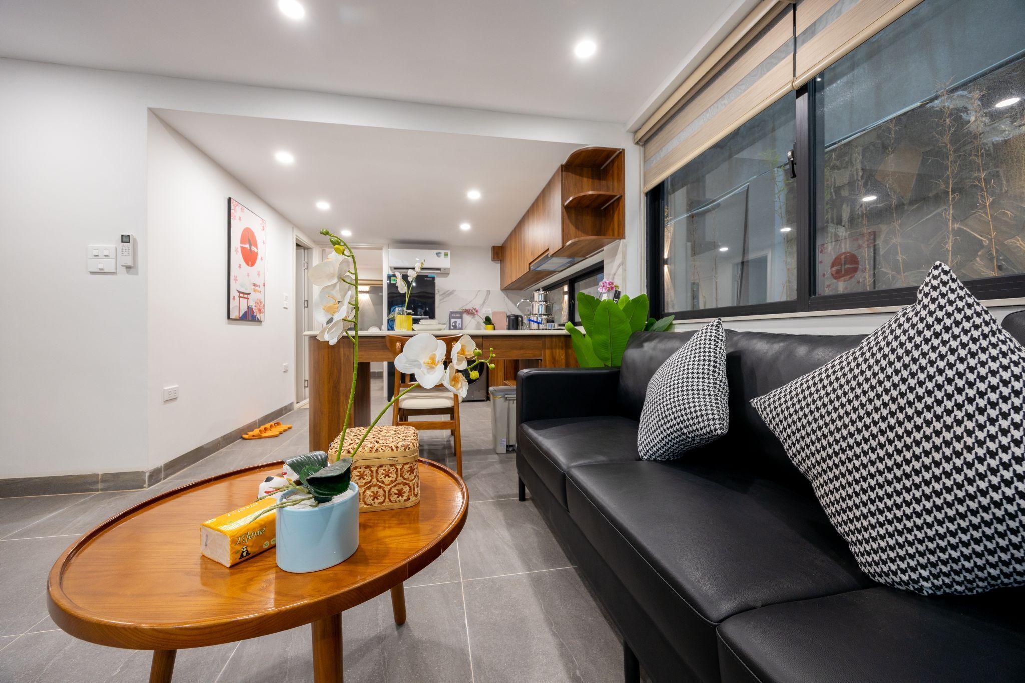 A modern living room with a black leather sofa, a wooden coffee table, and a kitchen in the background.
