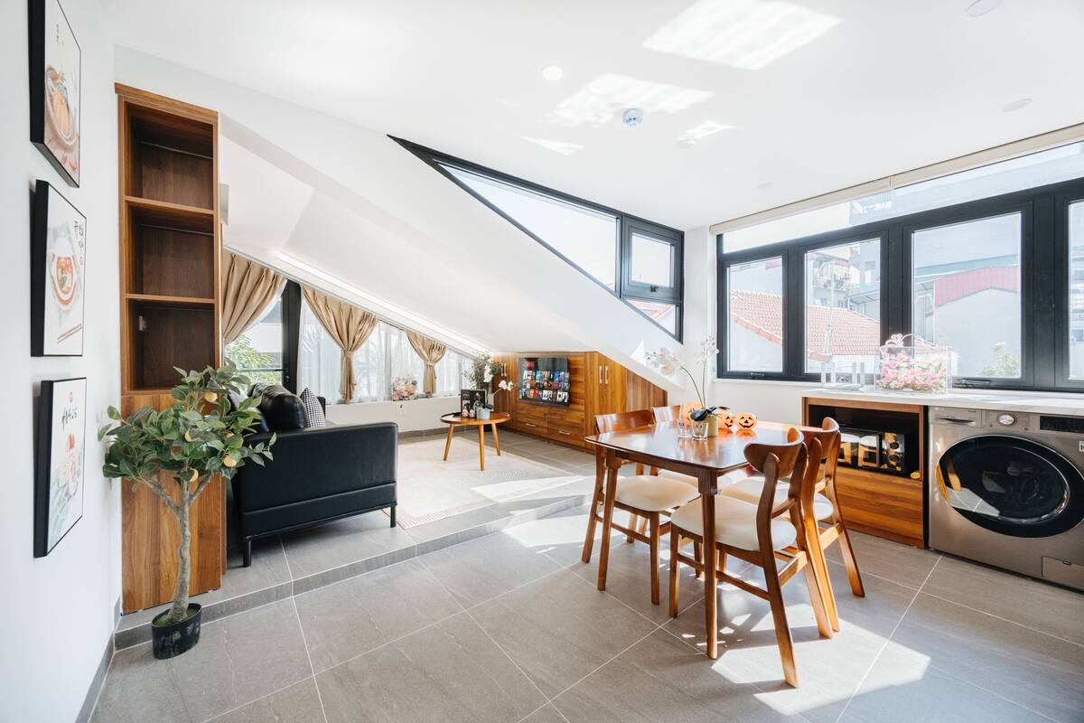 A modern kitchen with a dining area, built-in wooden shelves, and a washing machine.