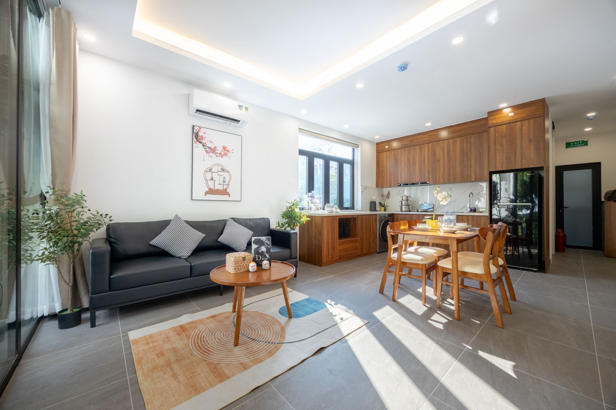 A modern living room with a sofa, coffee table, and dining area. There is a kitchen with wooden cabinets and a refrigerator.