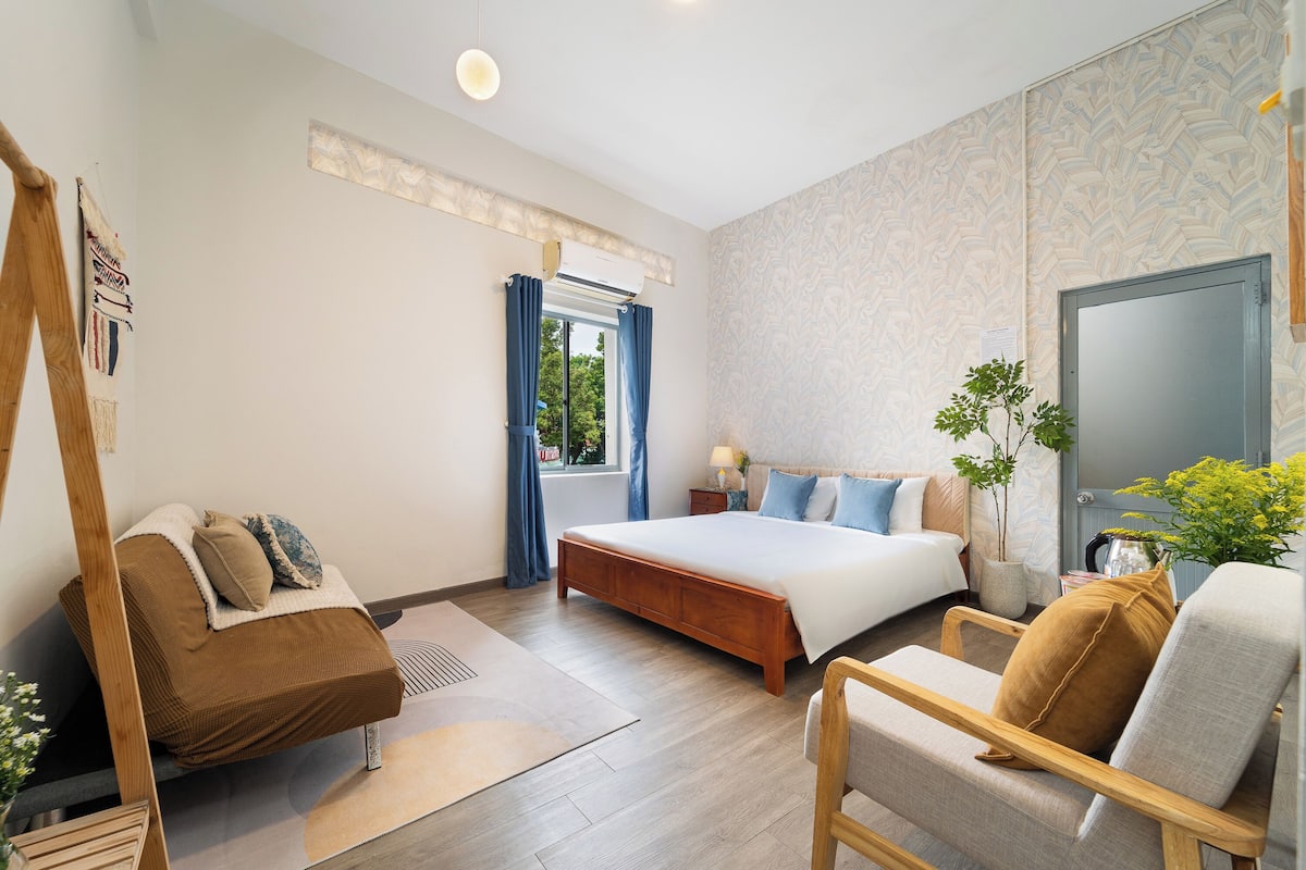 A modern bedroom with a large bed, a sofa, a chair, and a small table with a lamp.