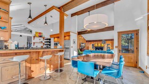 Une cuisine spacieuse avec un grand îlot central, des tabourets de bar et des chaises bleues disposées autour d’une table à manger en bois.