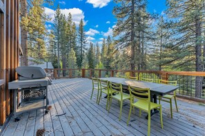 A deck with a grill, green chairs, and a table.