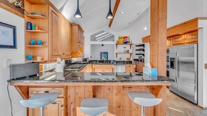 Une cuisine moderne avec des meubles en bois, un îlot central doté de tabourets, des appareils en acier inoxydable et un éclairage suspendu.