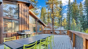 Une terrasse en bois avec une table et des chaises, entourée d’une balustrade en bois, donnant sur une zone boisée.