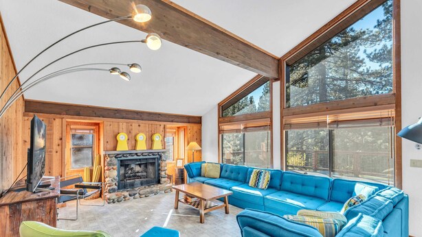 Un salon chaleureux avec un canapé bleu, des murs en bois, une cheminée et de grandes fenêtres.