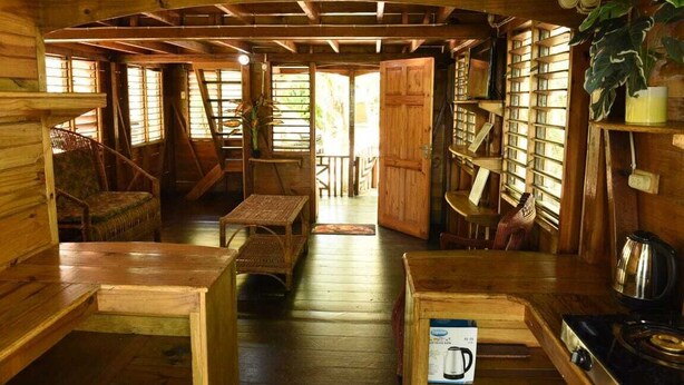 A wooden cabin interior with a dining area, kitchen, and bookshelves. - Take it easy at our eco friendly beach cabins where life meets nature funfilled  (Westmoreland)