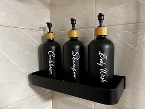 Three black bottles with gold caps on a black shelf against a tiled wall. - Cozy Escape In Rural Village (Barruelo de Santullan)