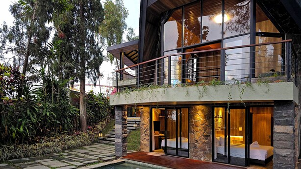 Een modern huis met twee verdiepingen, een zwembad, stenen muren en een balkon met planten.