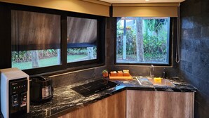 Een moderne keuken met een inbouwfornuis, een koffieapparaat en een spoelbak. Er zijn grote ramen met uitzicht op de tuin.