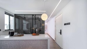 Cocina moderna con una isla central, puerta de vidrio que da a un comedor y una lámpara colgante.