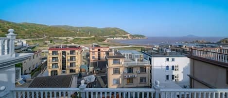 A terrace with potted plants, overlooking a coastal cityscape with buildings and a clear sky.