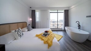 Una habitación de hotel moderna con una cama grande, una bañera y un balcón con vistas a la ciudad.