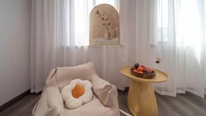Una habitación con un sofá color beige, una mesa redonda con fruta y un espejo con diseño floral.