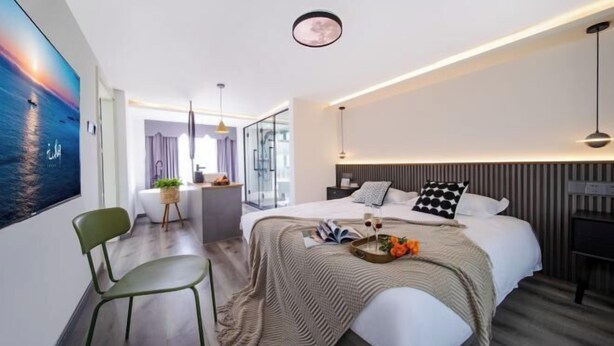 Una habitación de hotel moderna con una cama grande, un escritorio y una silla. Hay un cuadro en la pared, una lámpara en el techo y una ventana.
