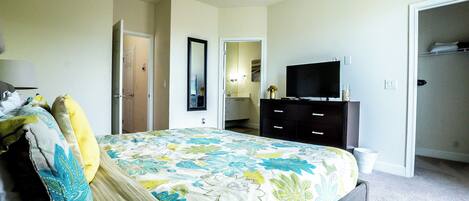 A bedroom with a bed, a dresser, a television, and an open closet.