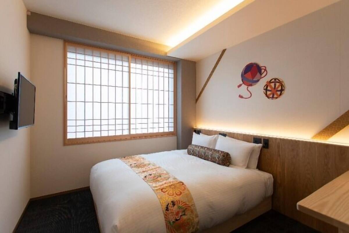 Una cama bien tendida con una colcha decorativa, una ventana con persianas de madera y adornos en la pared.