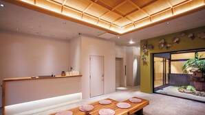 A modern interior with a reception desk, a wooden bench with round cushions, and a small indoor garden.