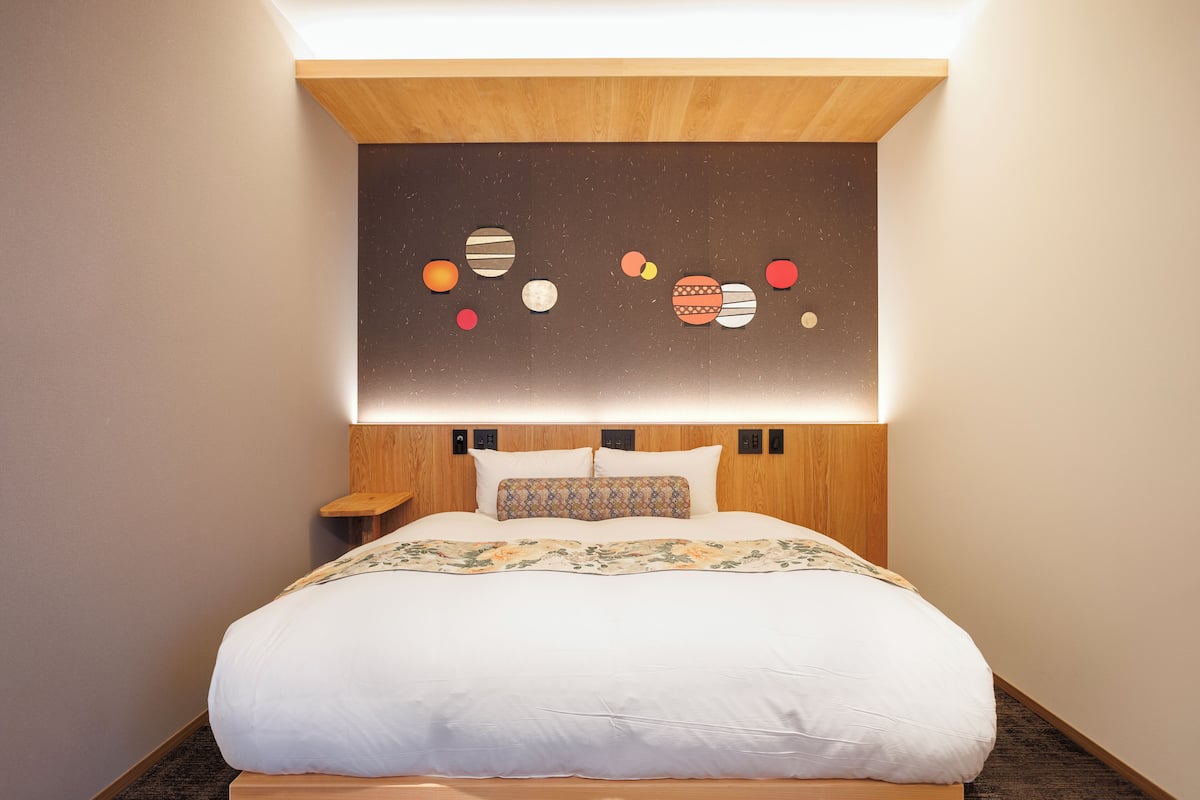Un dormitorio moderno con una cama grande, un cabecero con iluminación integrada y una obra de arte en la pared que representa planetas.