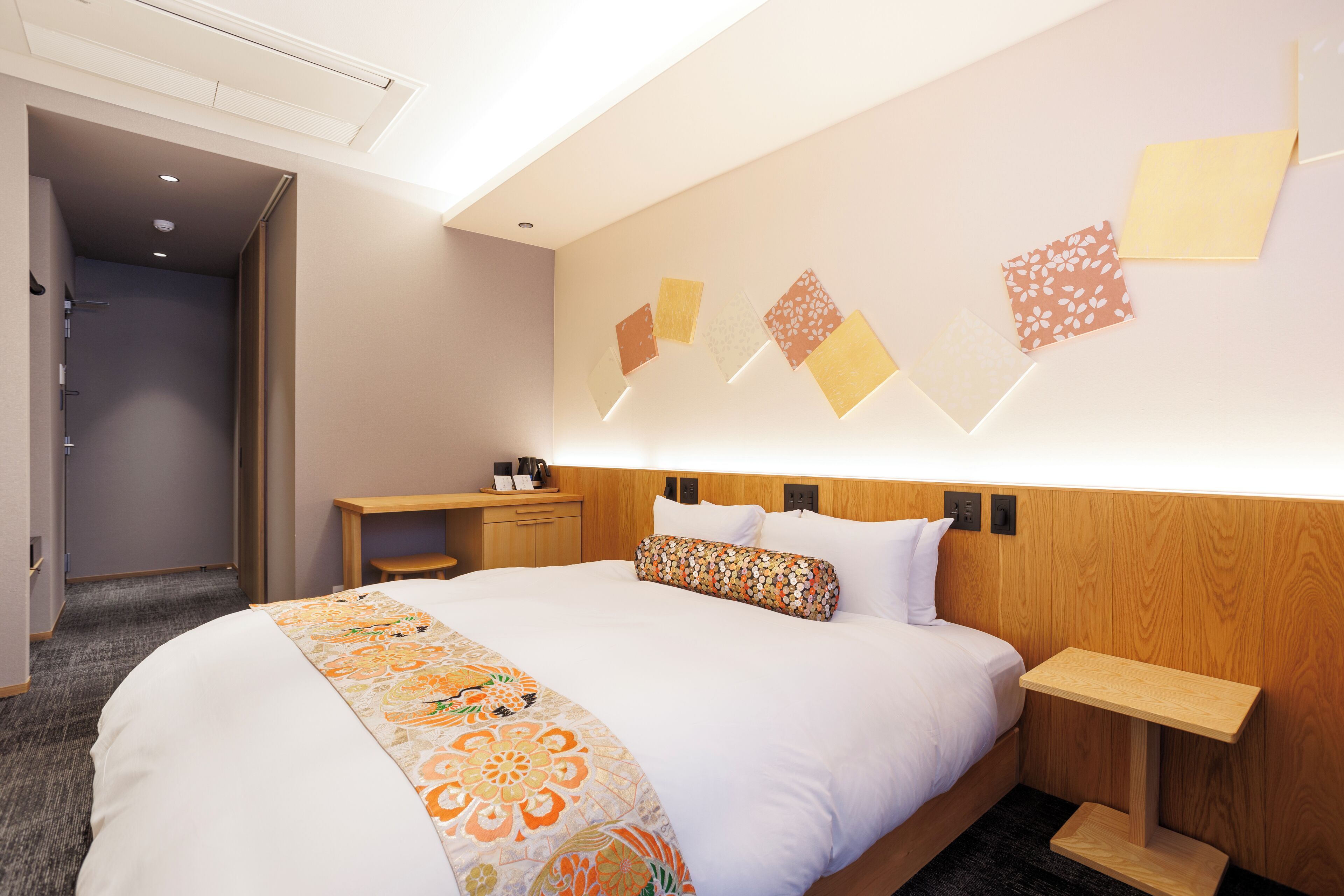 A hotel room with a large bed, a wooden headboard, a bedside table, and a wall with decorative panels.