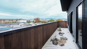 A modern building with a wooden balcony, a view of the cityscape, and a rooftop garden with rocks and a sculpture.