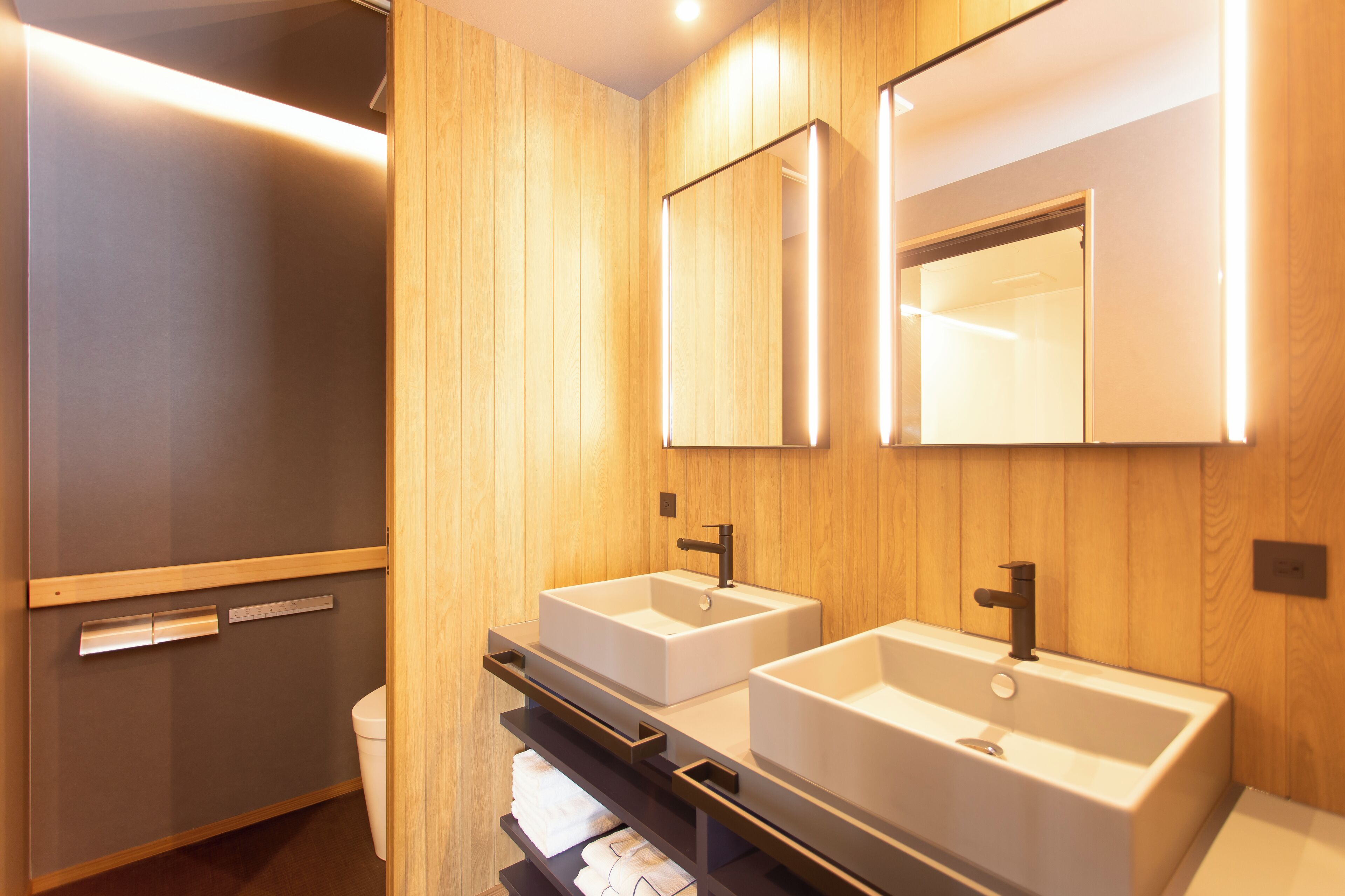 Un baño moderno con dos lavamanos, paneles de madera y un espejo.