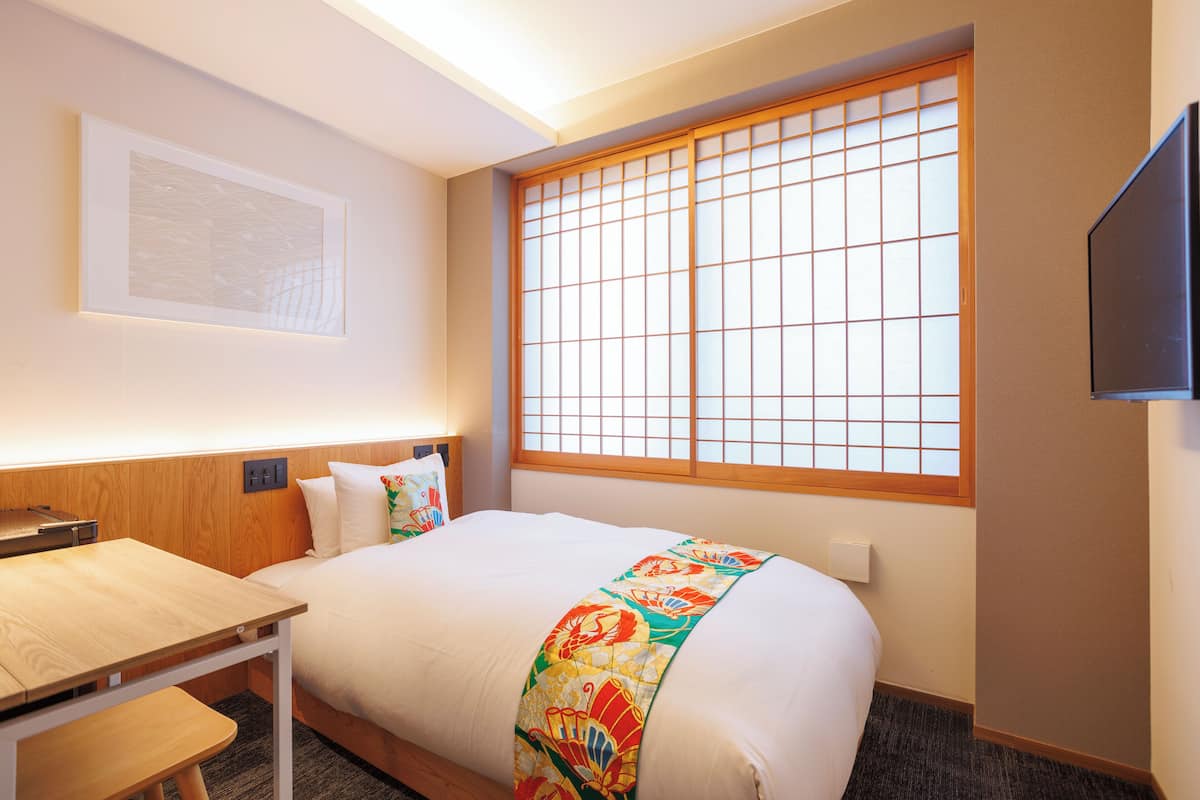 Una habitación de hotel con una cama, un escritorio, una silla, un televisor y una ventana con vistas.