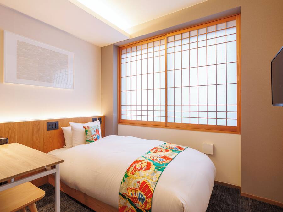 A hotel room with a bed, a desk, a chair, a TV, and a window with a view.