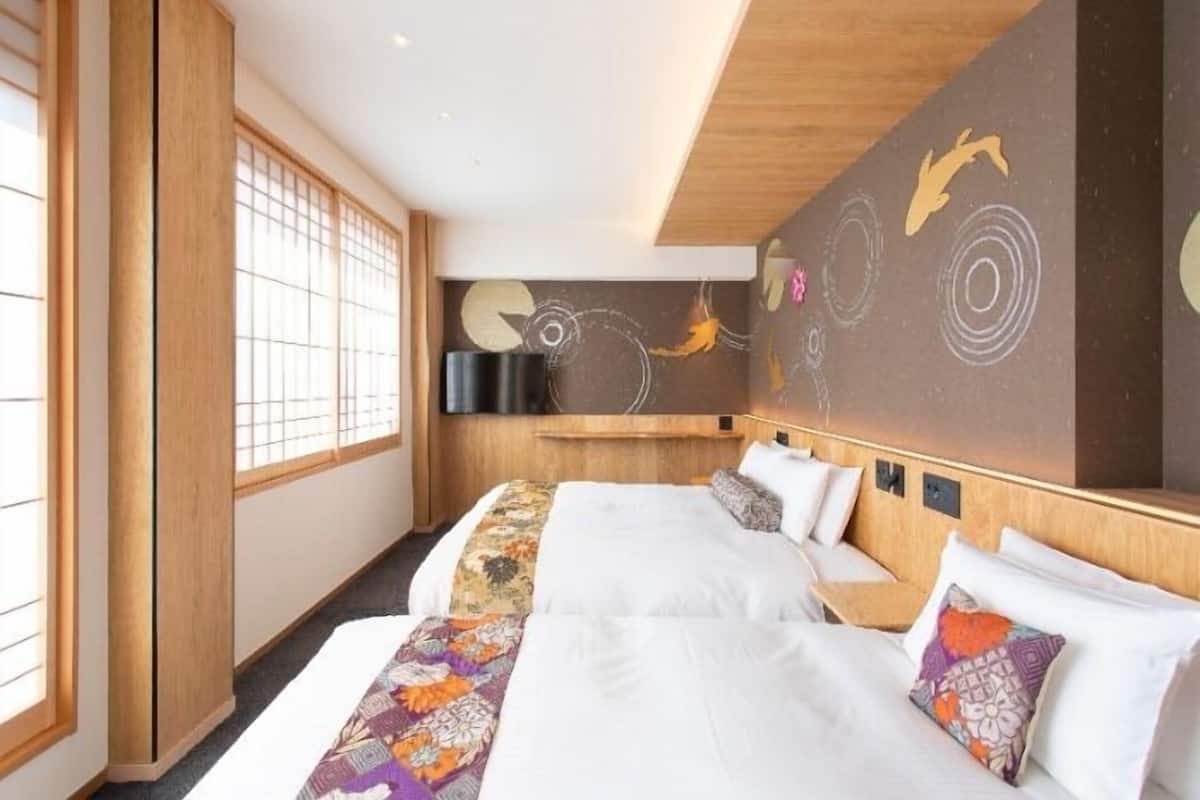 Una habitación de hotel con un ventanal grande, una cama con ropa de cama blanca, una colcha de colores y una pared decorada con arte abstracto.