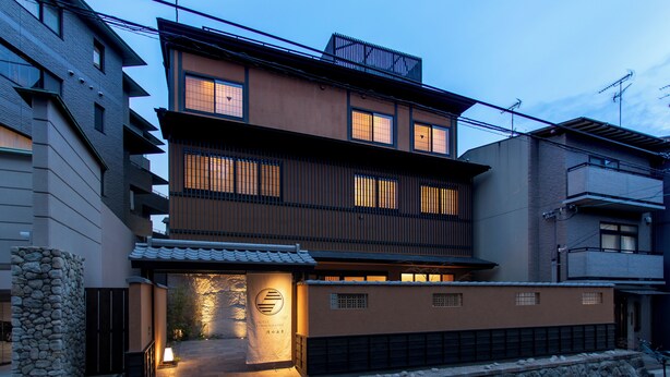 A multi-story hotel with a traditional facade, a stone wall, and a well-lit entrance.