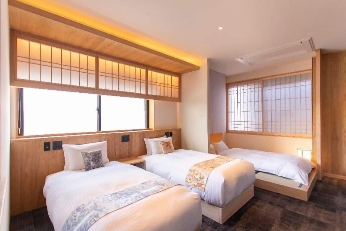 Habitación de hotel con dos camas, cabeceros de madera y ventanas amplias con celosías de estilo tradicional.