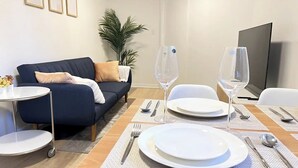 Un coin repas avec une table dressée pour deux personnes, un canapé, une télévision et une plante.