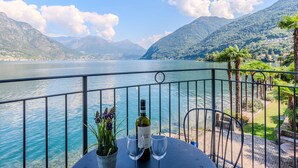 A table with a bottle of wine and two glasses, overlooking a lake with mountains in the background. - Nice apartment for 4 people with WIFI, TV and balcony (Osteno)