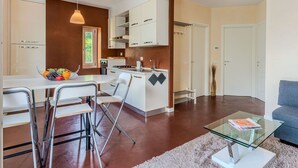 A modern kitchen with white cabinets, a dining area with a glass table, and a living room with a sofa. - Nice apartment for 4 people with WIFI, TV and balcony (Osteno)
