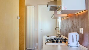 A compact kitchen with a gas stove, a kettle, and a radiator. - Cosy apartment for 4 people with WIFI, TV and balcony (Osteno)