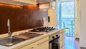 A modern kitchen with a gas stove, sink, and oven. There is a balcony with a view of the outdoors. - Cosy apartment for 4 people with WIFI, TV and balcony (Osteno)