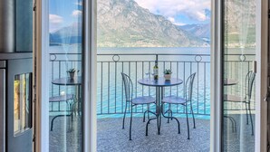 A balcony with a table and chairs overlooking a lake with mountains in the background.