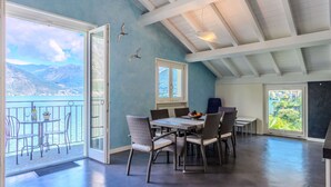 A dining area with a table and chairs, a view of the mountains, and a balcony with a railing.