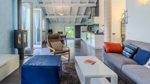A modern living room with a sofa, armchair, and coffee table, a fireplace, and a kitchen area in the background.