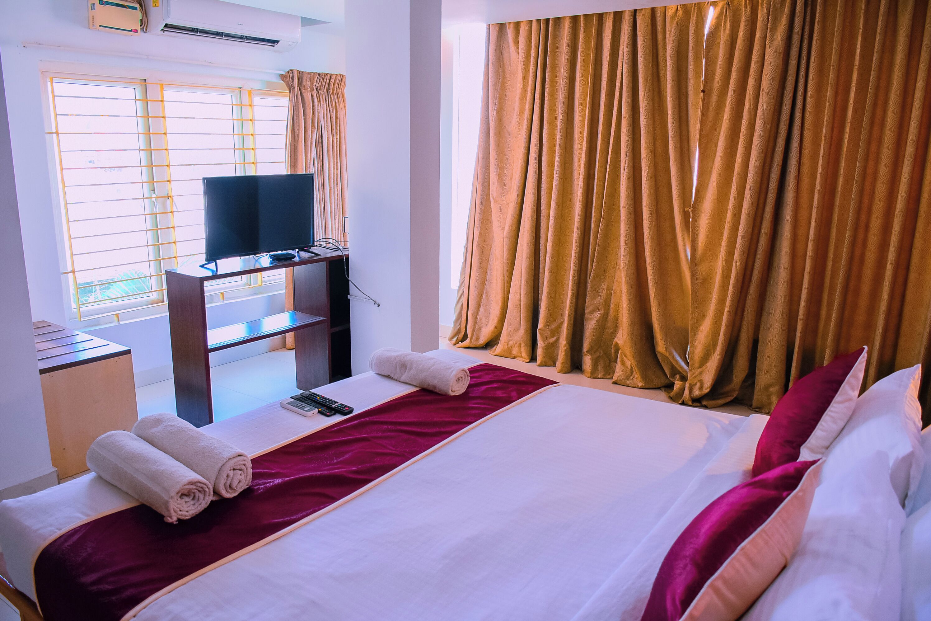 A hotel room with a bed, a television on a desk, and a window with curtains.