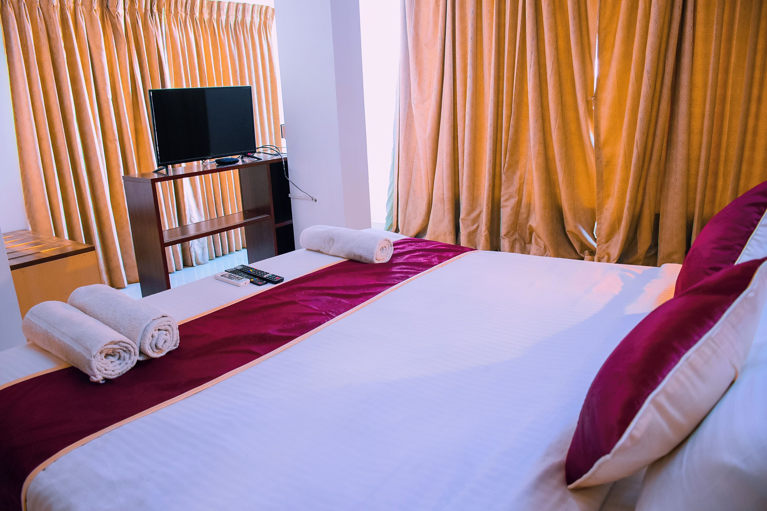 Une chambre d’hôtel avec un lit soigneusement fait, un téléviseur à écran plat posé sur un meuble en bois et un bureau avec un téléphone.
