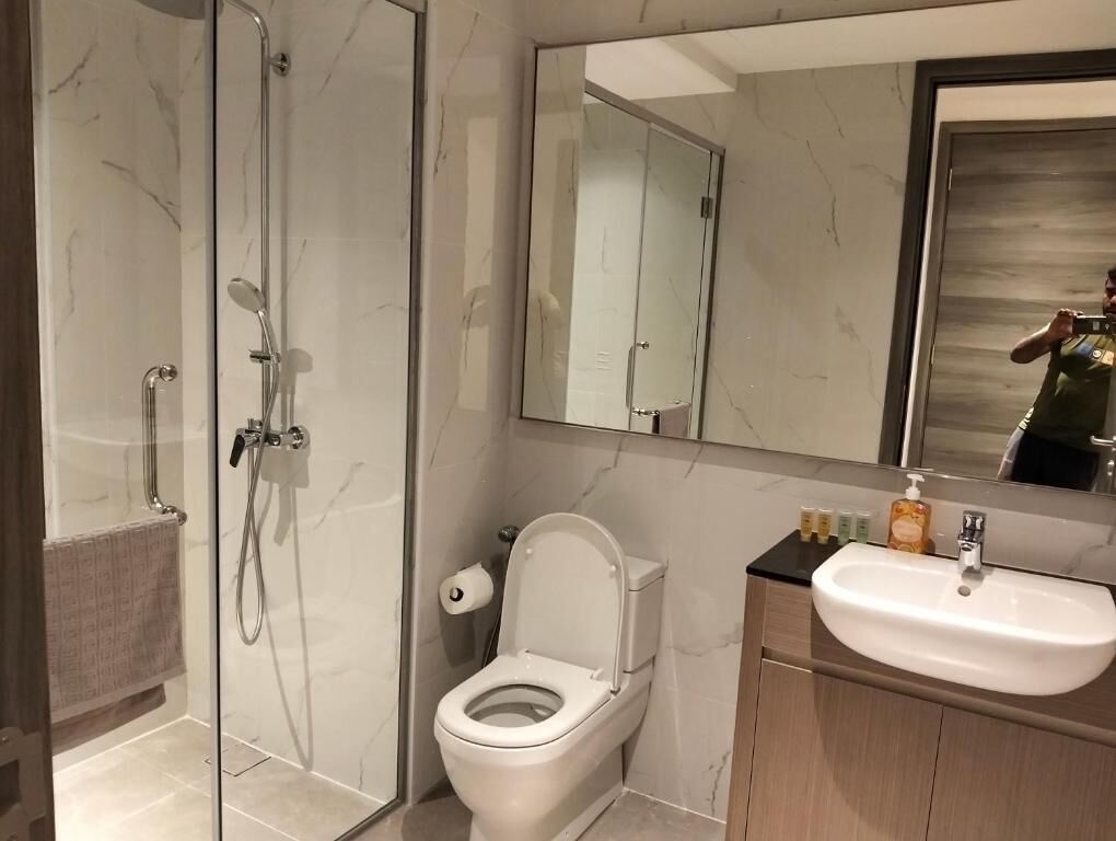 A modern bathroom with a glass shower enclosure, a toilet, and a sink with a mirror above.