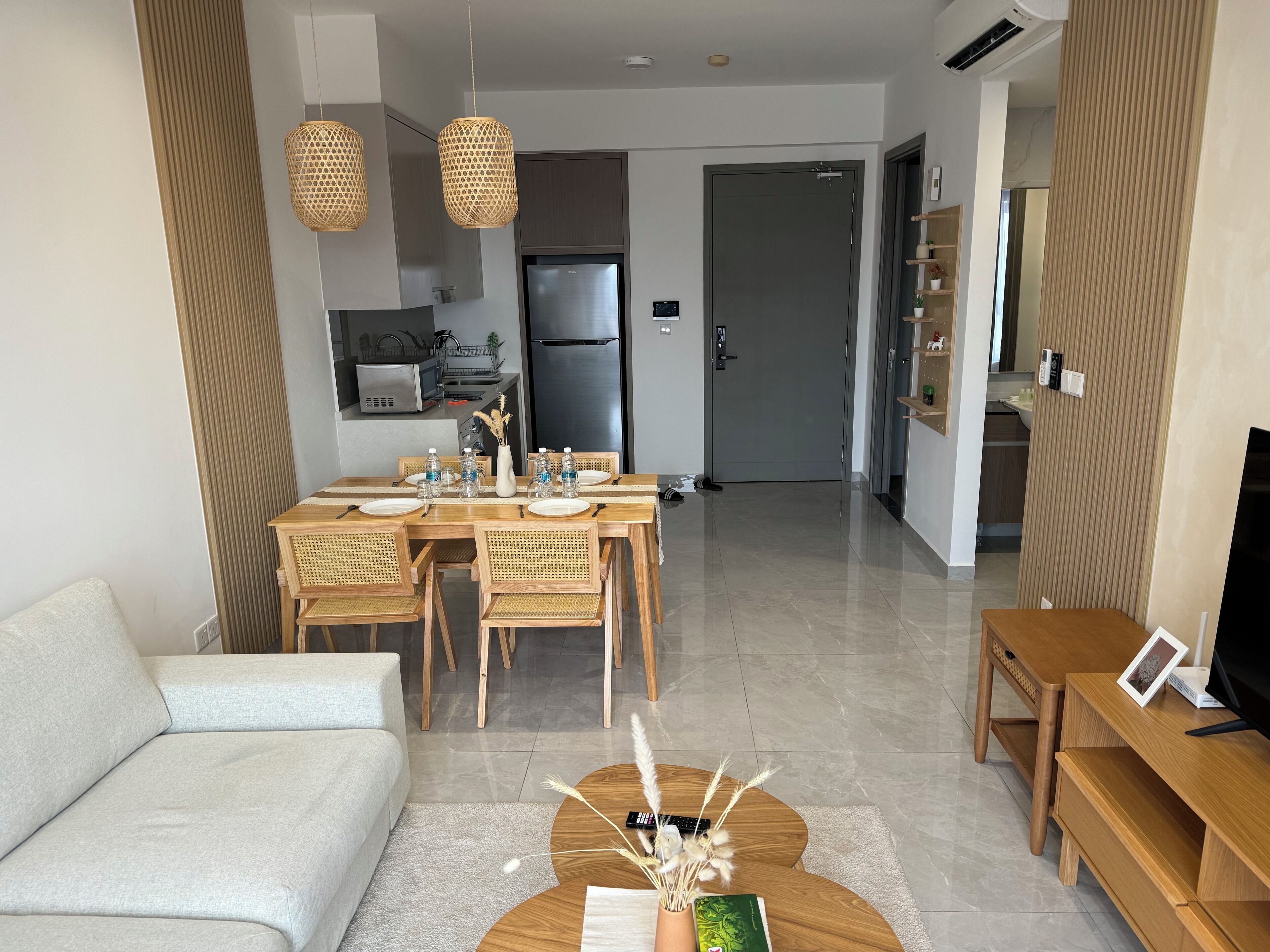 A modern living room with a sofa, coffee table, and TV stand. A dining area with a table and chairs is visible in the background.