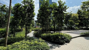 A paved walkway with lush greenery and tall trees, leading towards modern buildings in the background. - Agile Premium Service Suite KL (Kuala Lumpur)