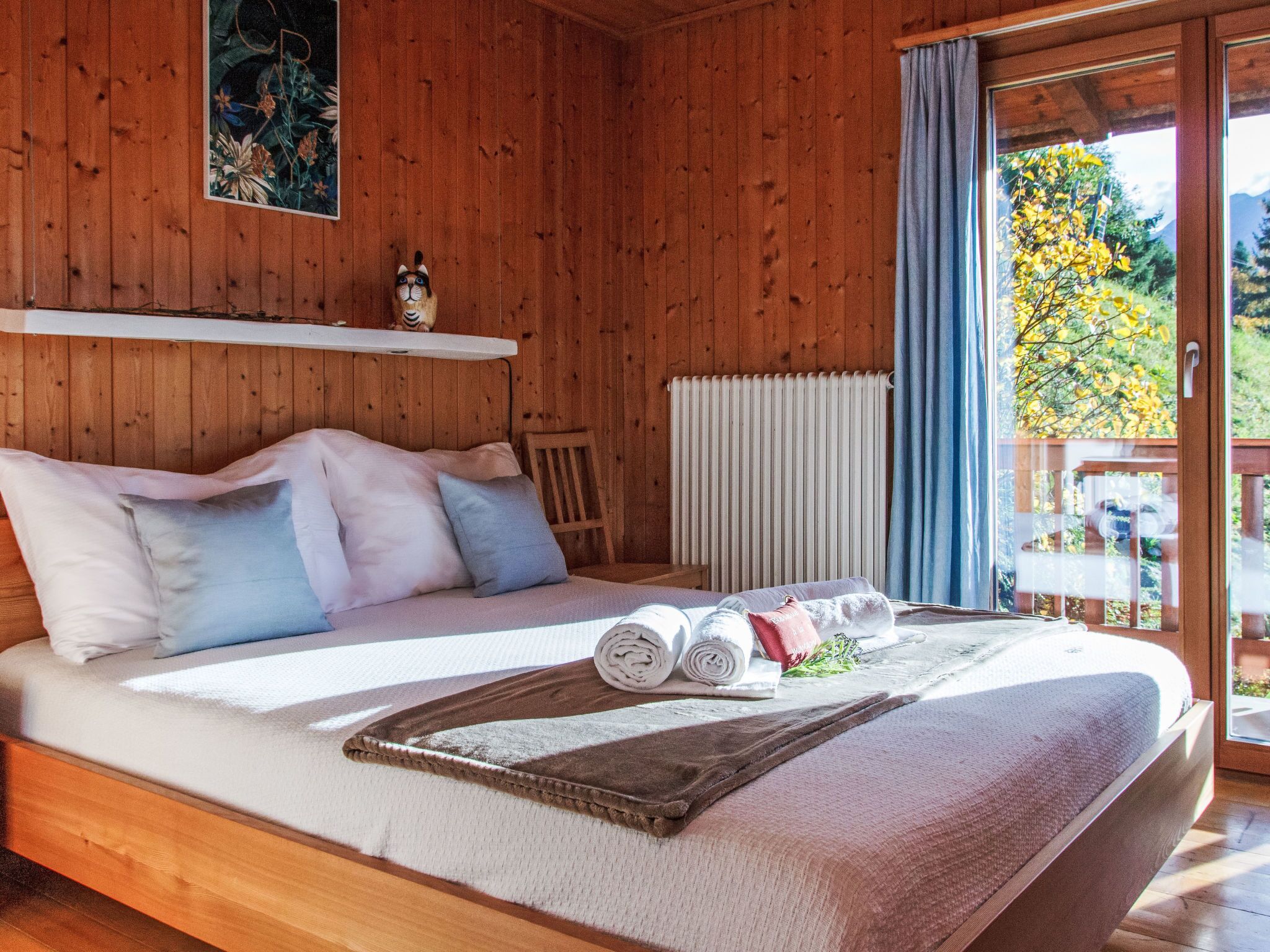 A wooden cabin bedroom with a bed, pillows, a rolled towel, and a blanket.