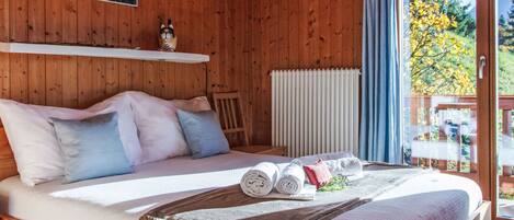 A wooden cabin bedroom with a bed, pillows, a rolled towel, and a blanket.