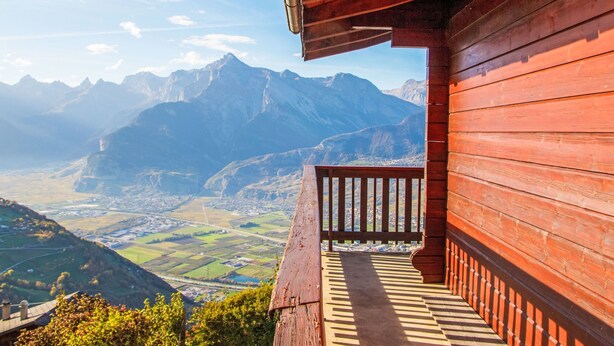 Une cabane en bois dotée d’un balcon donnant sur un paysage montagneux.