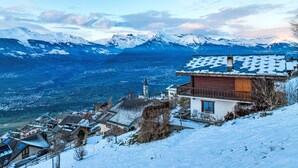 Un village de montagne enneigé, avec une église imposante et un bâtiment de style chalet doté d’un toit en pente.