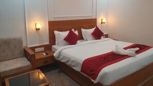 Een hotelkamer met een bed, nachtkastje, stoel en een klein tafeltje.