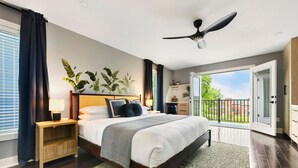 Une chambre à coucher comprenant un lit, des tables de chevet, un ventilateur de plafond, une grande fenêtre et une vue sur l’extérieur.